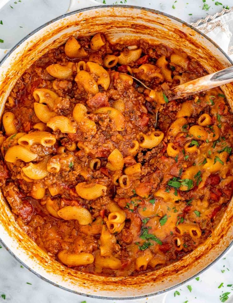 american goulash in a beige dutch oven with a ladle inside.