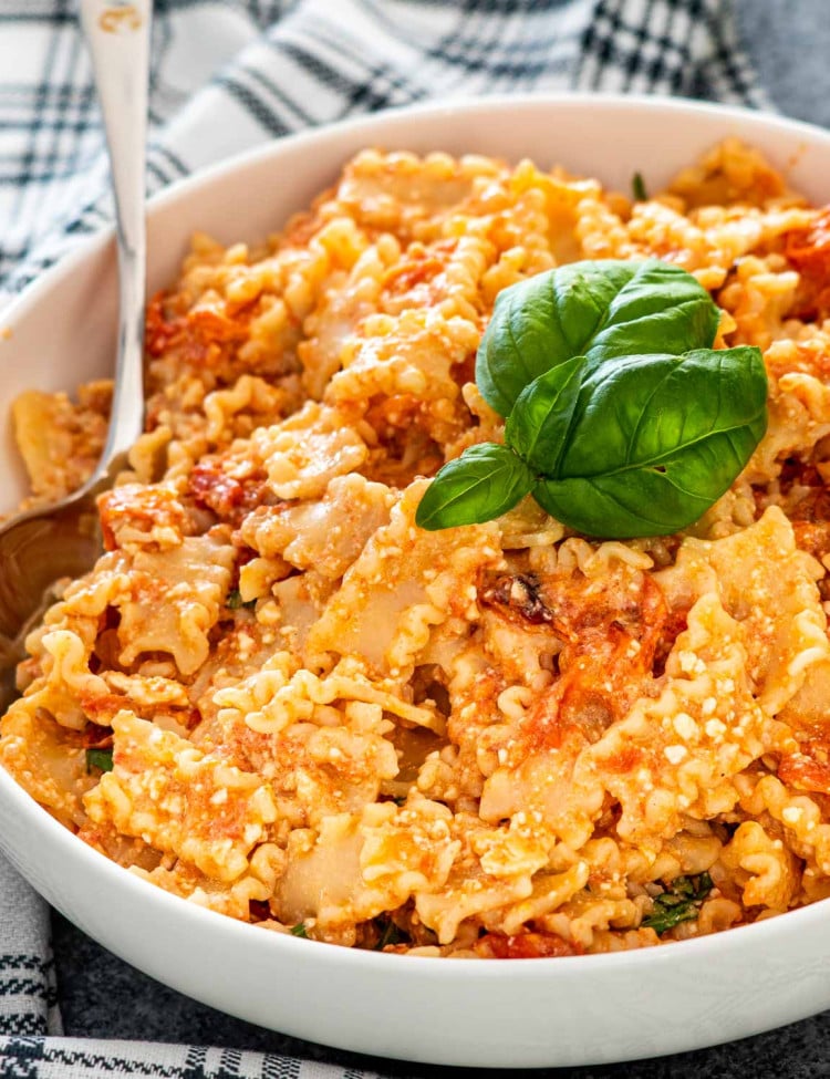 baked feta pasta in a white bowl garnished with fresh basil.