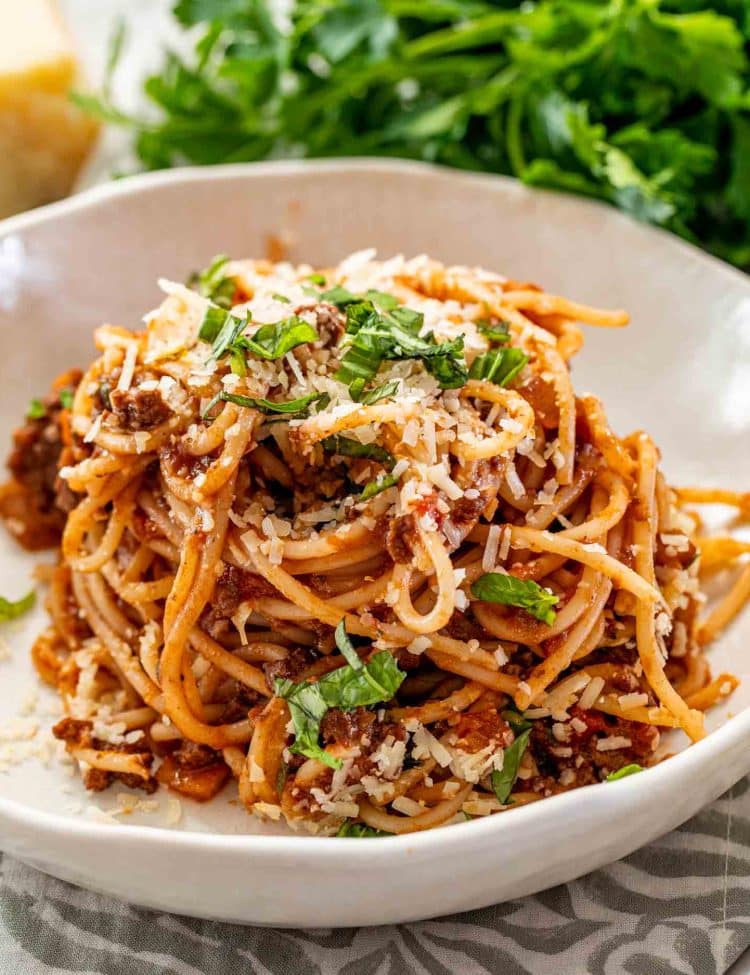 a serving of spaghetti bolognese in a white bowl garnished with parsley.