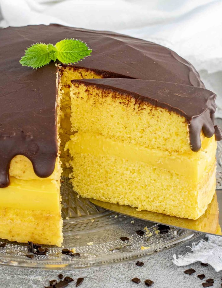 A Boston Cream Pie with sponge cake layers, creamy filling, topped with rich chocolate ganache and garnished with fresh mint.