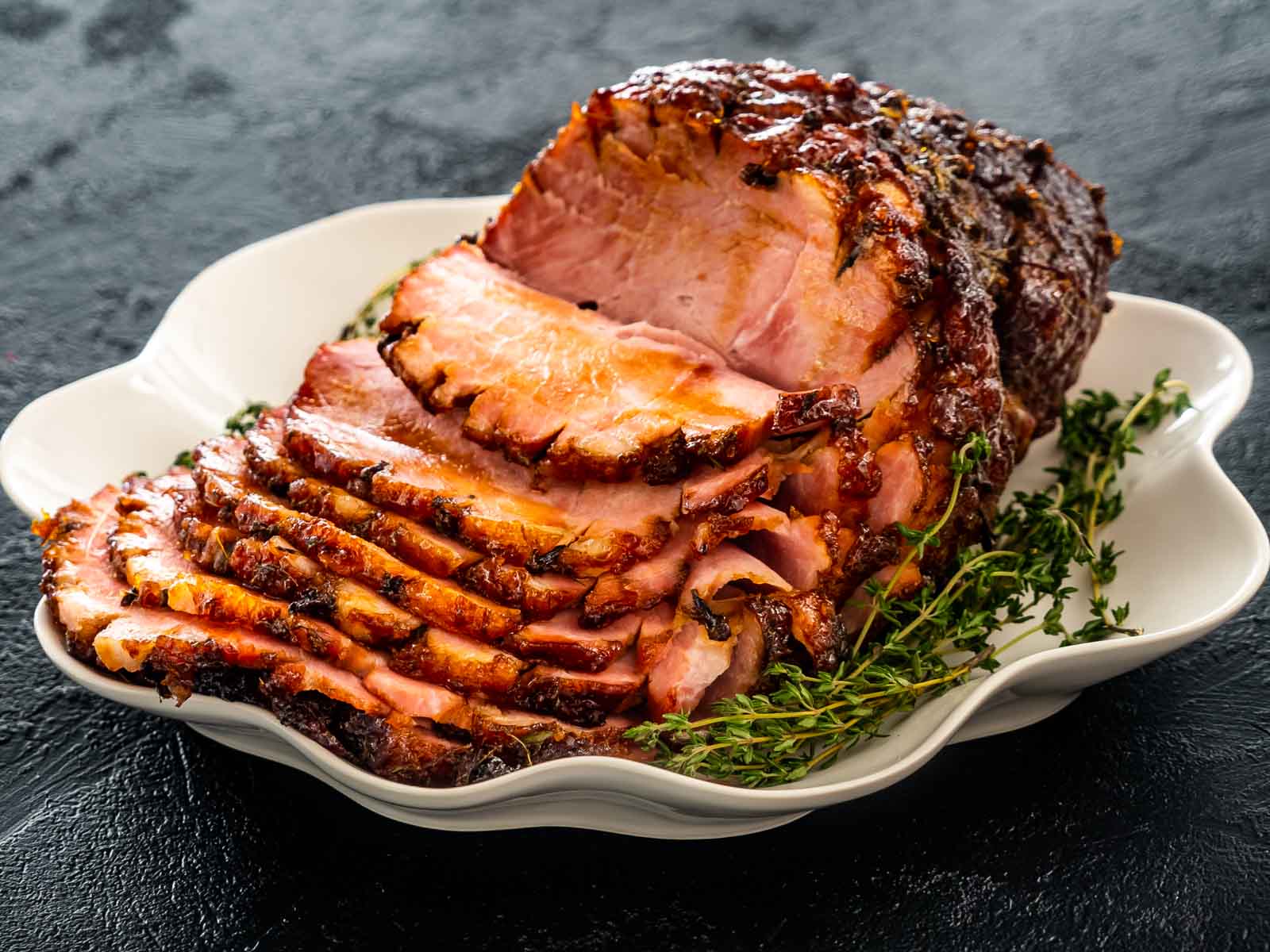 bourbon glazed ham on a white platter sliced garnished with fresh thyme.