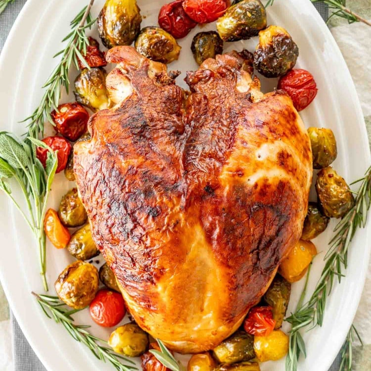 a brined roast turkey breast on a turkey platter garnished with veggies and fresh herbs.