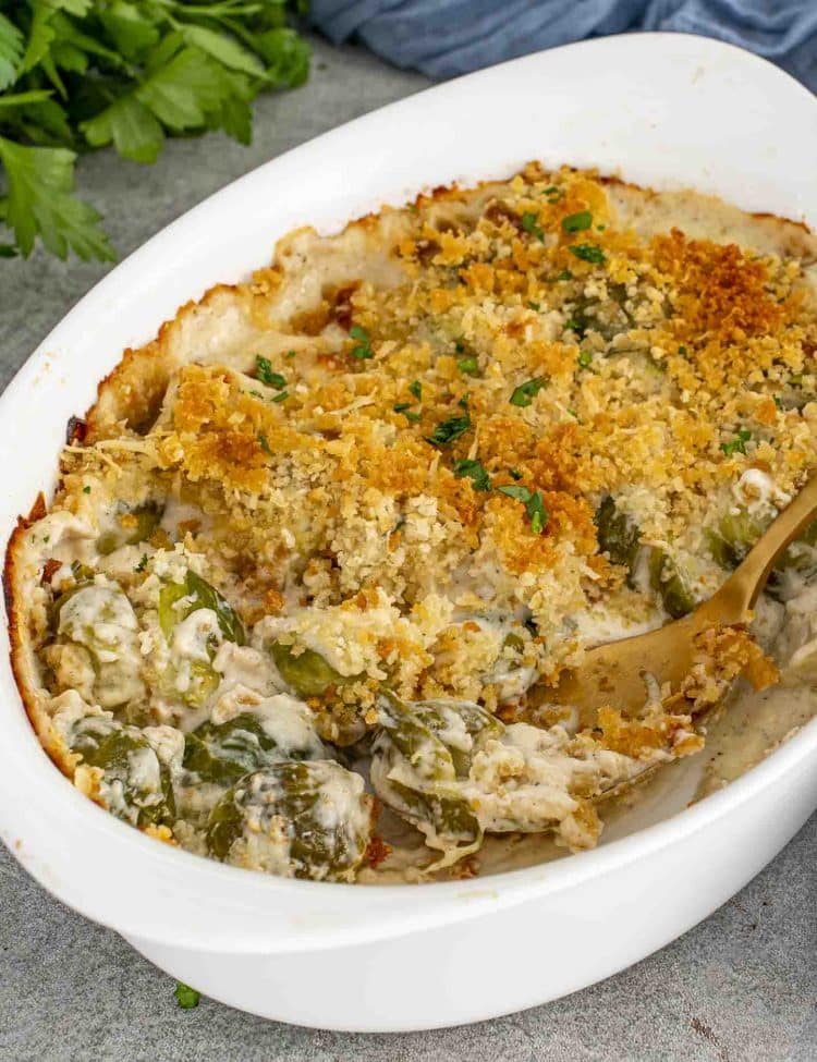 Golden brown Brussels sprouts gratin in a white baking dish with creamy sauce and crispy panko topping, served with gold spoon.