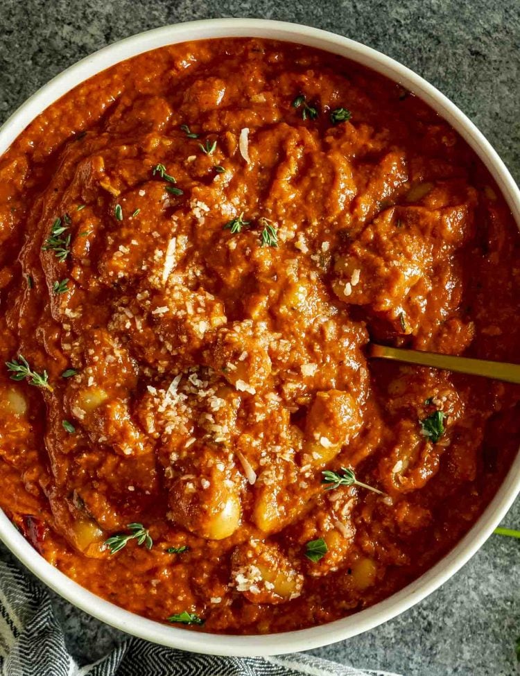 Close-up of creamy tomato butter beans with visible butter beans, tomato sauce, Parmesan, and fresh thyme garnish.