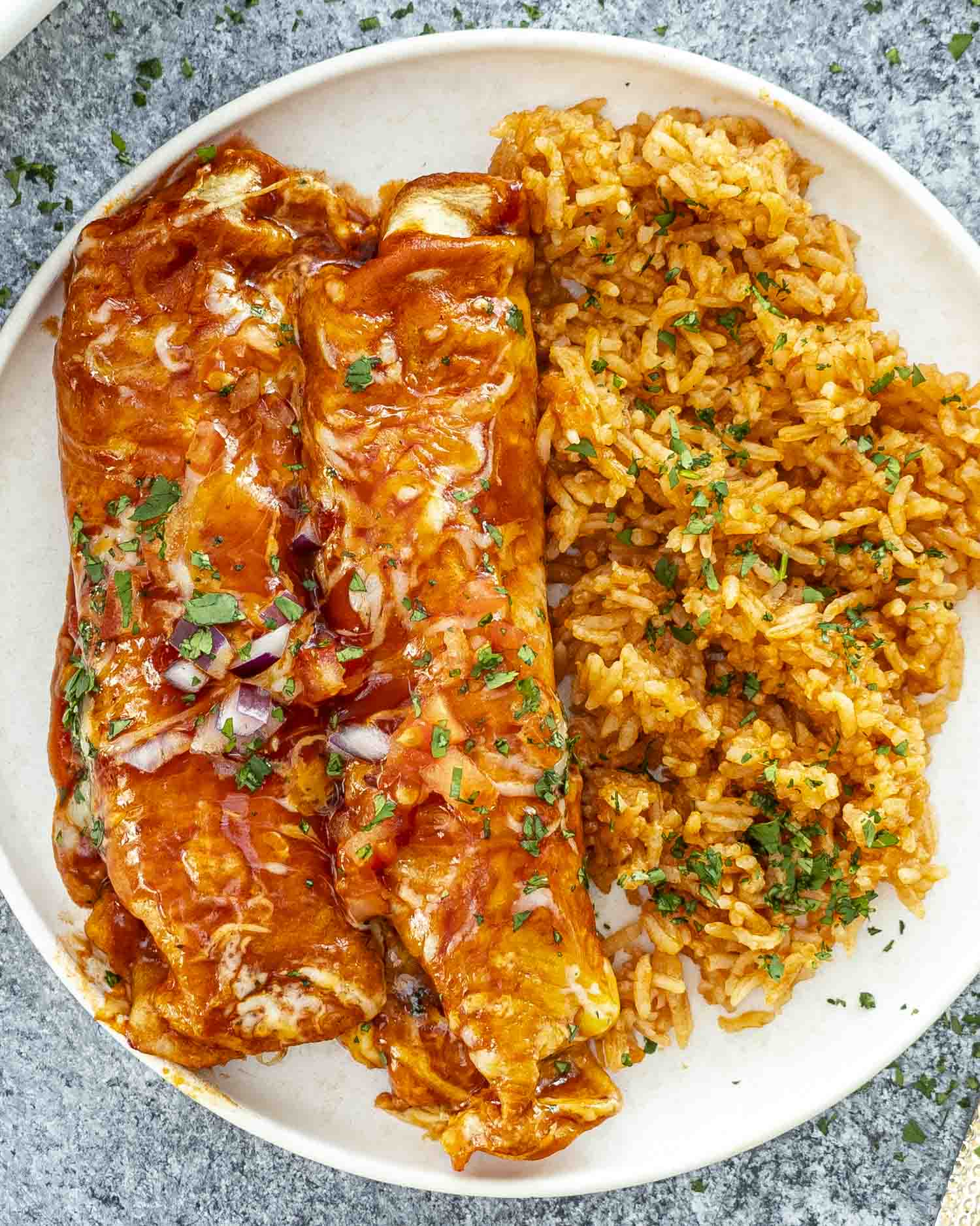 Overhead view of chicken enchiladas with rice, sprinkled with chopped parsley on a rustic stone surface.