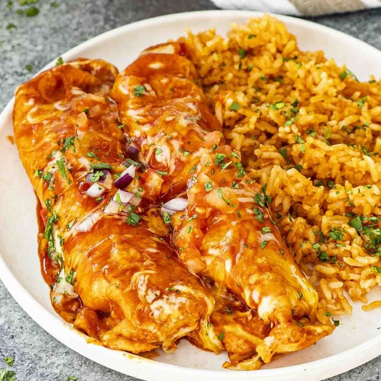 Two saucy chicken enchiladas plated with Mexican rice, garnished with fresh herbs on a white plate.