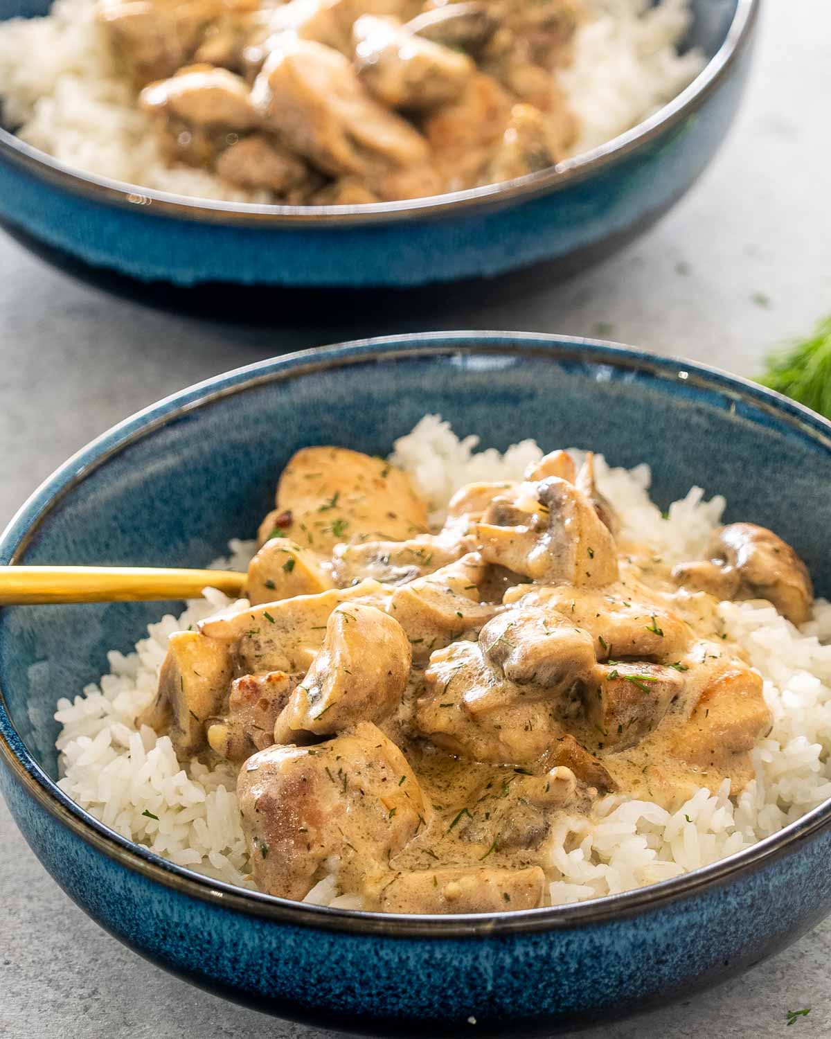 chicken and mushroom in creamy dill sauce over a bed of rice in a blue bowl.