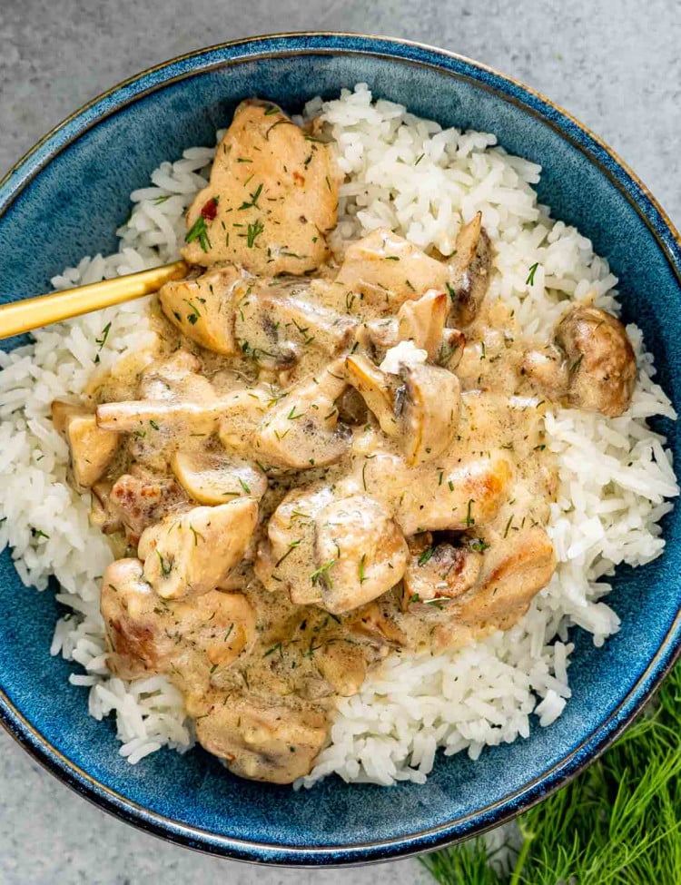 chicken and mushroom in creamy dill sauce over a bed of rice in a blue bowl.