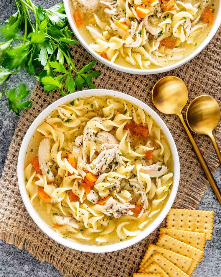 freshly made chicken noodle soup in 2 white bowls.