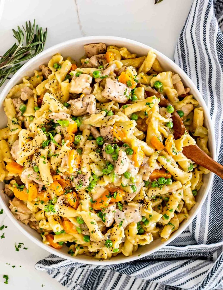 chicken pot pie pasta in a white serving bowl with a wooden serving spoon.