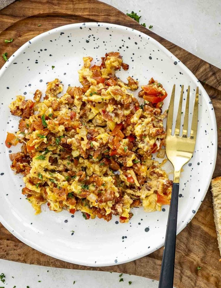Chorizo and eggs scramble plated with golden fork, topped with chopped parsley, served with rustic bread on the side.
