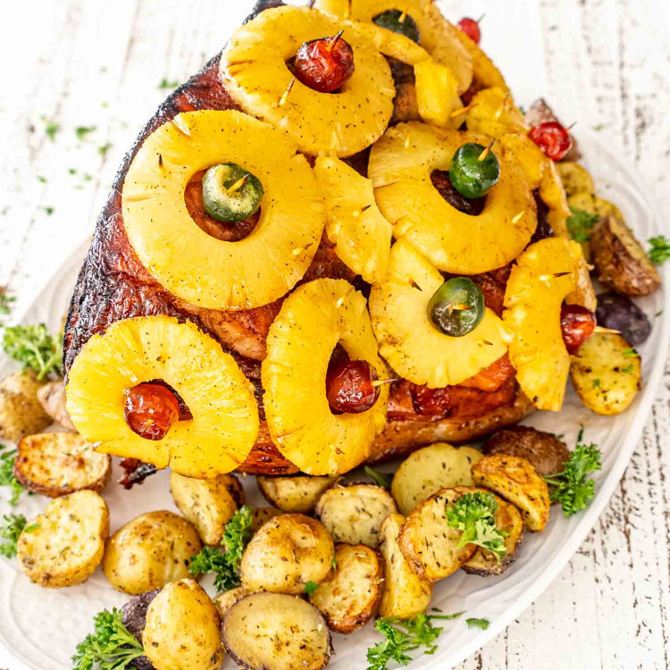 a whole christmas ham fresh out of the oven on a white serving platter.