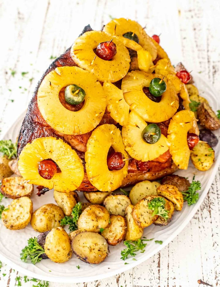 a whole christmas ham fresh out of the oven on a white serving platter.