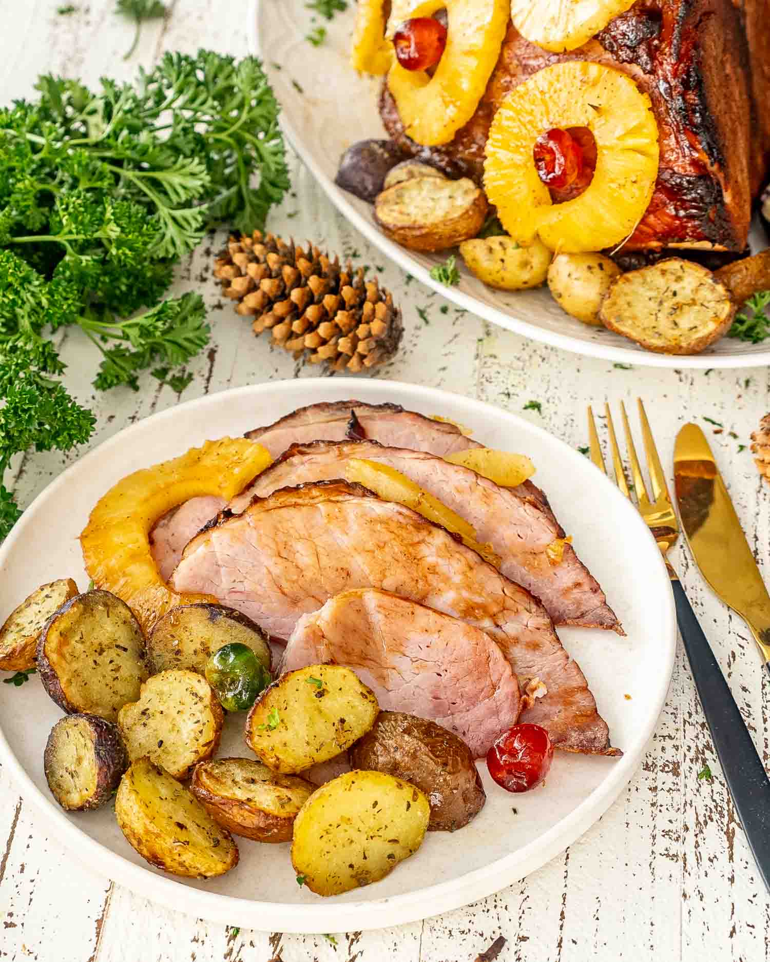 sliced up christmas ham on a white plate along some roasted potatoes.