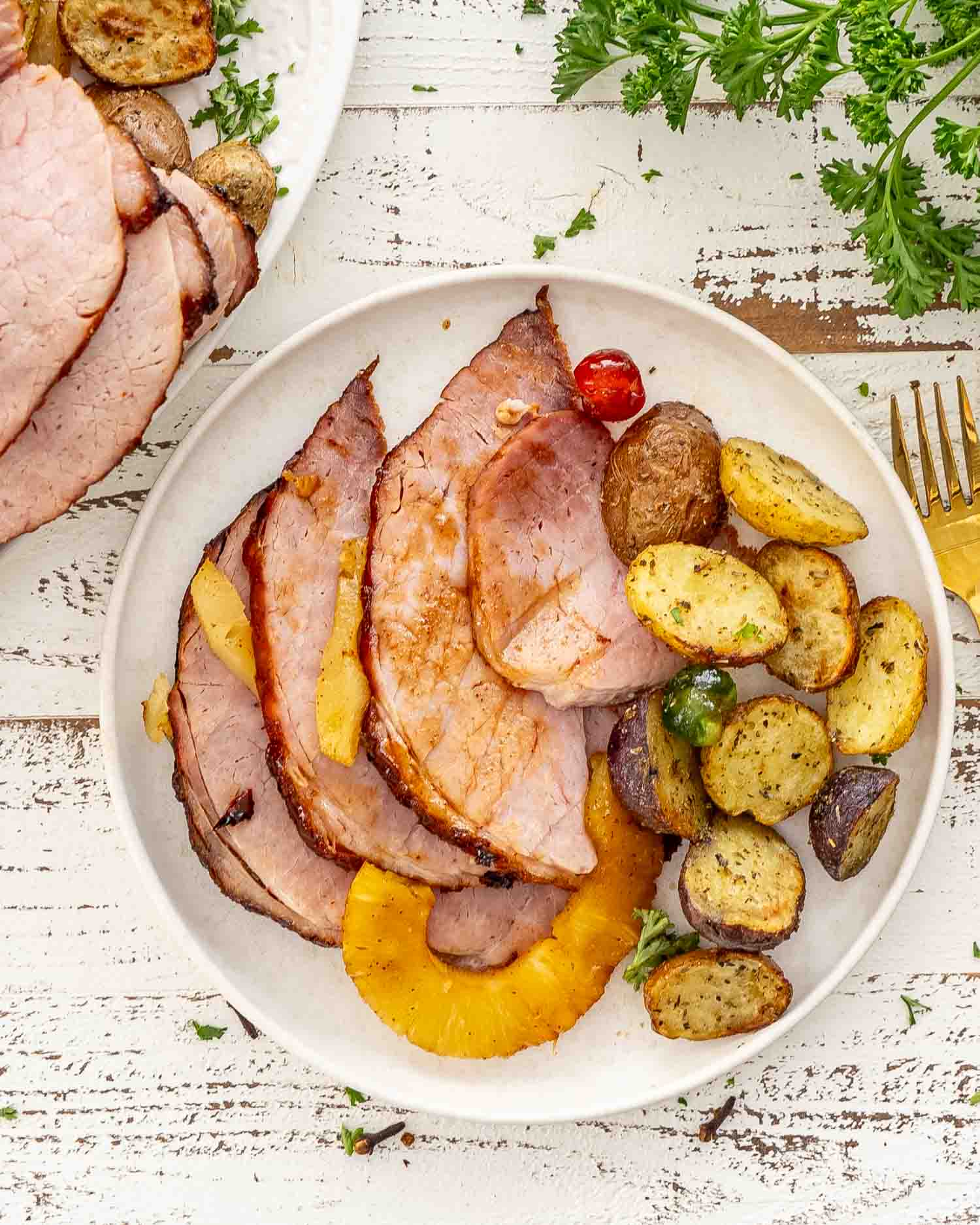 sliced up christmas ham on a white plate along some roasted potatoes.