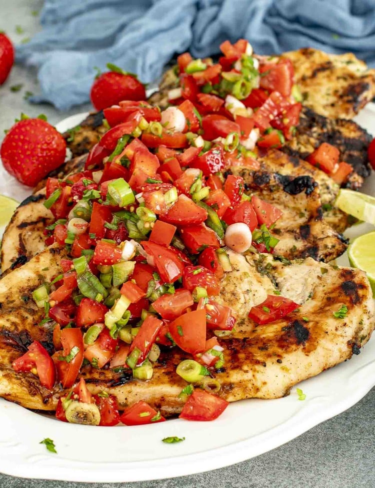 Grilled Cilantro Lime Chicken topped with a vibrant strawberry salsa, served on a white platter with fresh lime wedges and whole strawberries as garnish.