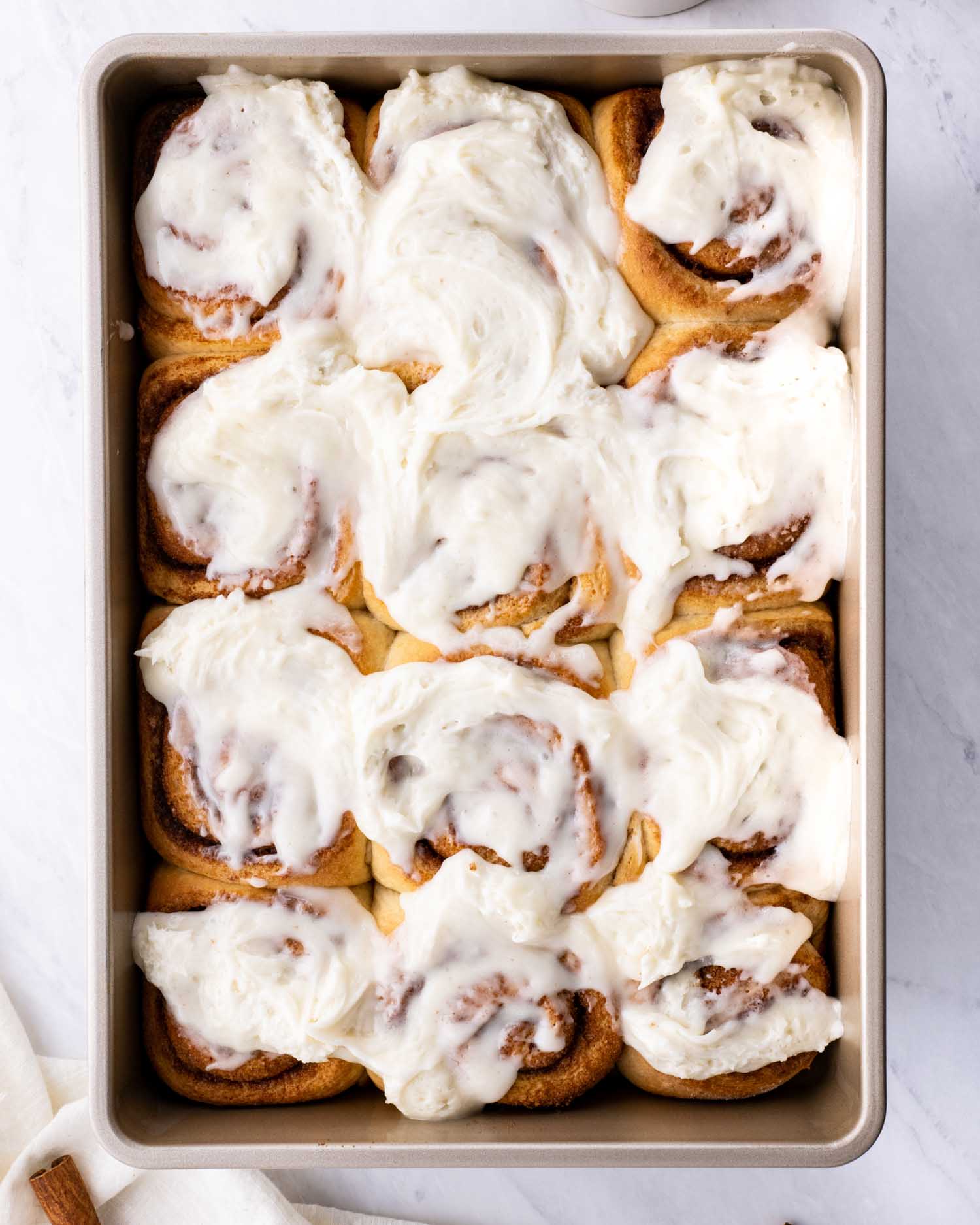 freshly baked cinnabon cinnamon rolls in a baking dish with cream cheese icing.