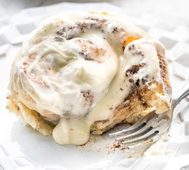 side view shot of a cinnamon bun with a bite taken out of it on a plate