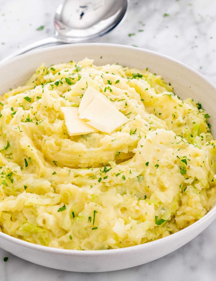 a big white bowl full of colcannon topped with butter.