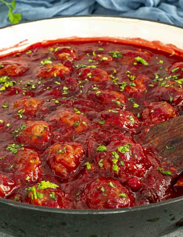 Cranberry meatballs simmering in a skillet with thick, glossy cranberry sauce and sprinkled parsley on top.