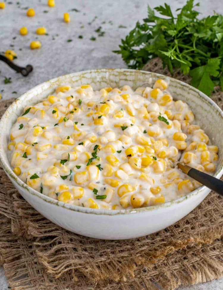 Homemade creamed corn served in a rustic ceramic bowl, garnished with fresh parsley for an easy holiday side.