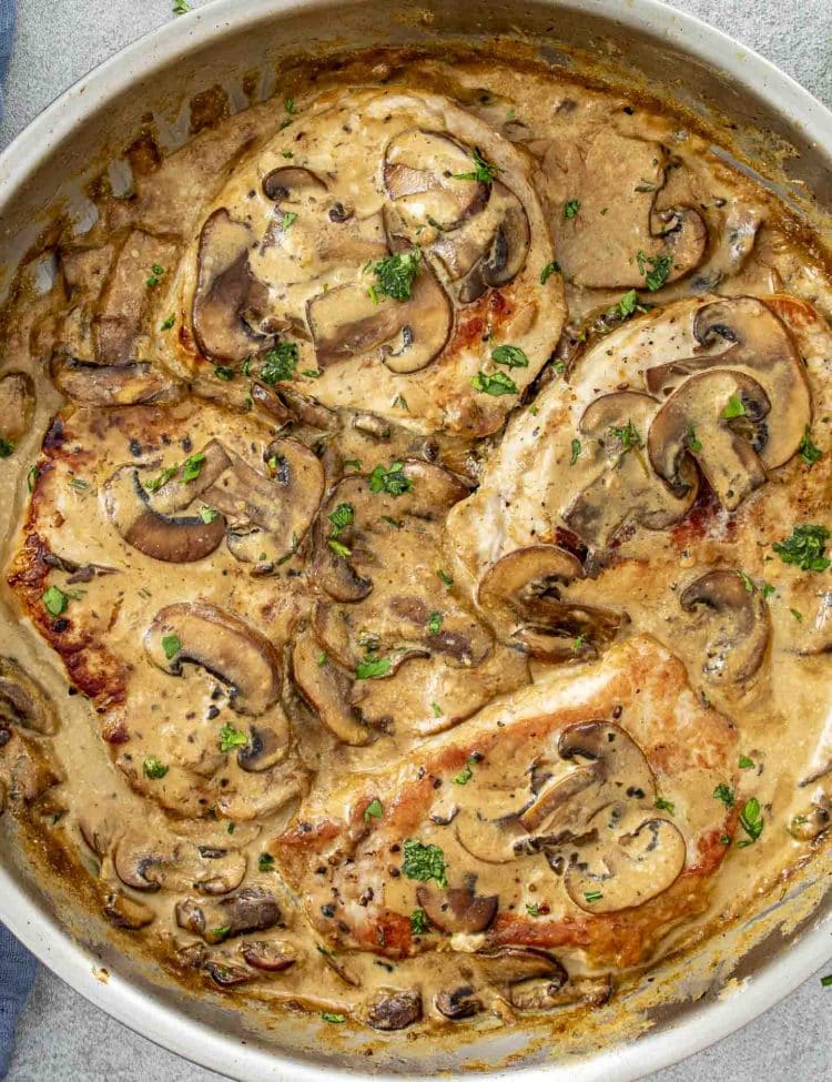 Overhead view of creamy Dijon mushroom pork chops cooked in a rich sauce with fresh herbs and mushrooms.