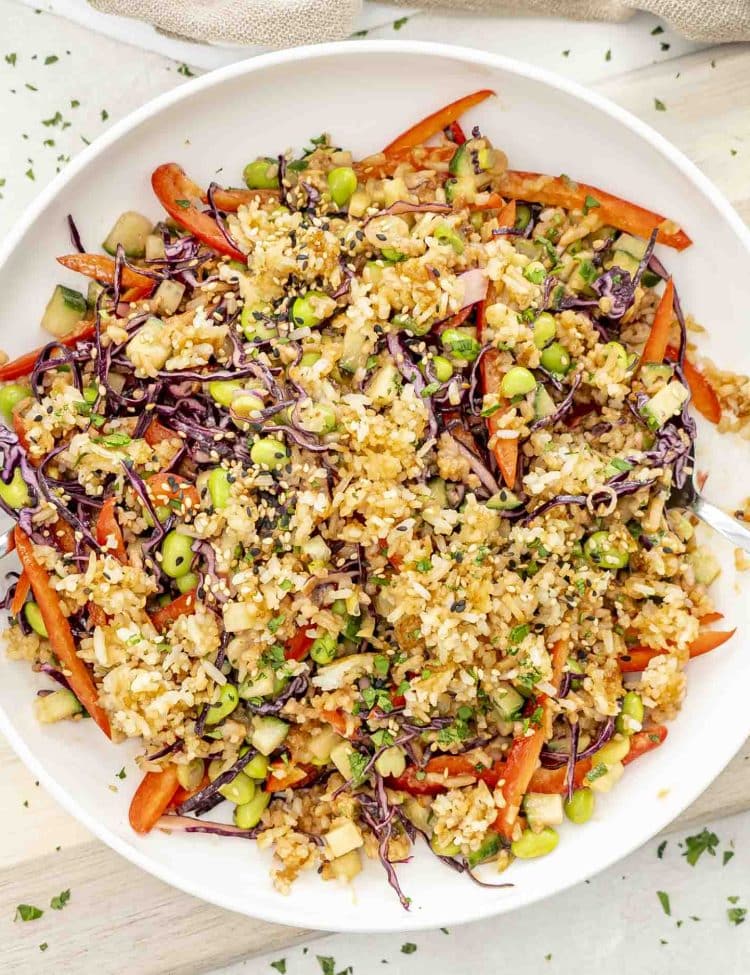 Top view of crispy rice salad in a white bowl with colorful veggies, herbs, and crunchy golden rice clusters.