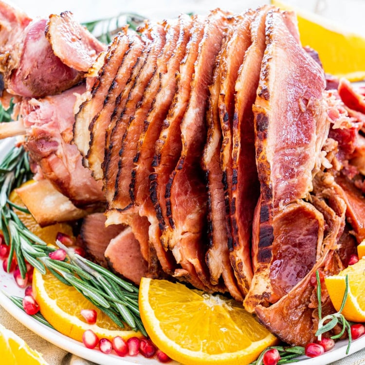 side view shot of a sliced ham on a plate with rosemary, orange wedges and pomegranate seeds