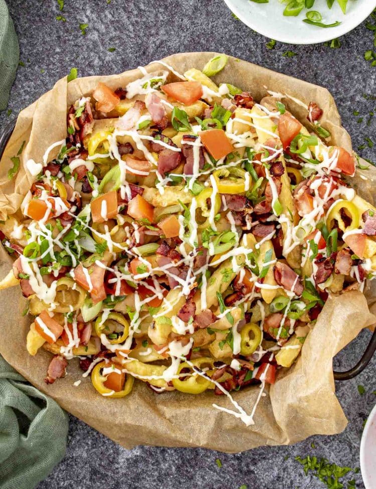 Overhead view of loaded dirty fries with bacon, banana peppers, fresh tomatoes, green onions, and mayonnaise drizzle.