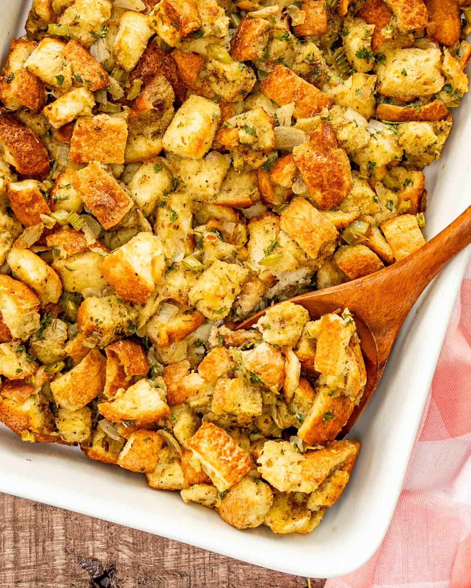 freshly baked bread stuffing in a white casserole dish with a wooden spoon inside.