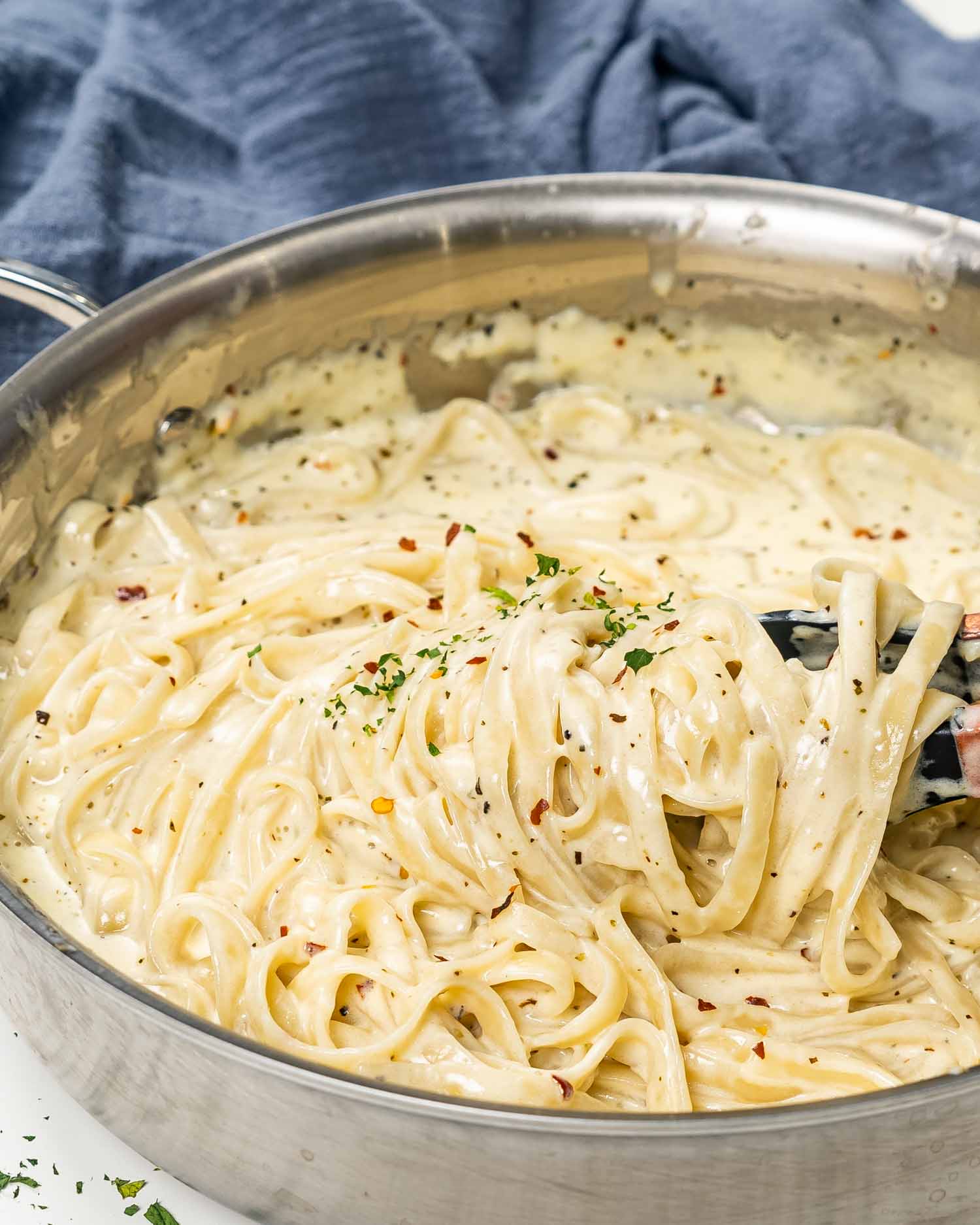 freshly made fettuccine alfredo in a skillet garnished with red pepper flakes and parsley.