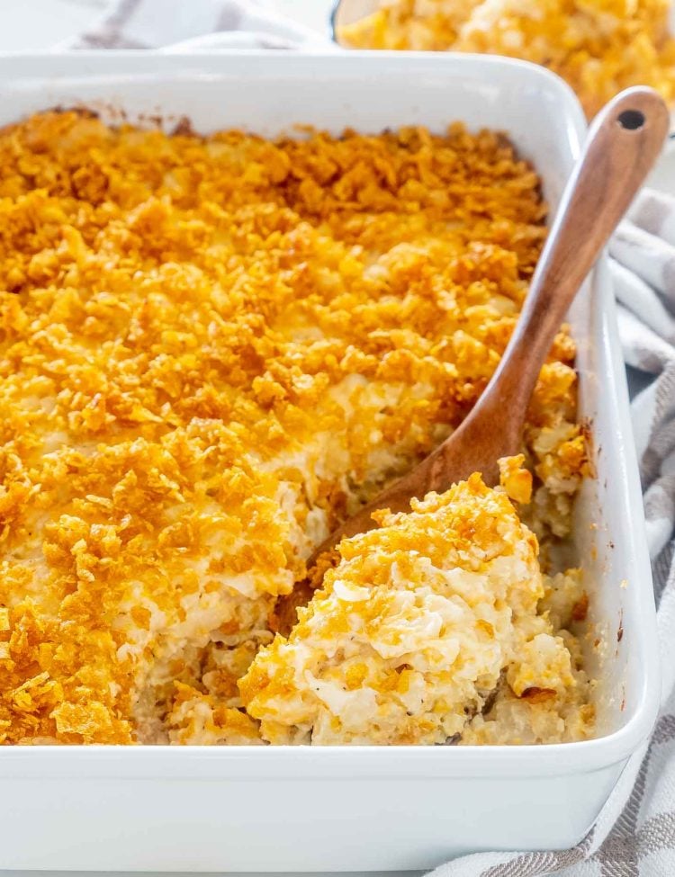 funeral potatoes freshly baked in a casserole dish with a wooden serving spoon inside.