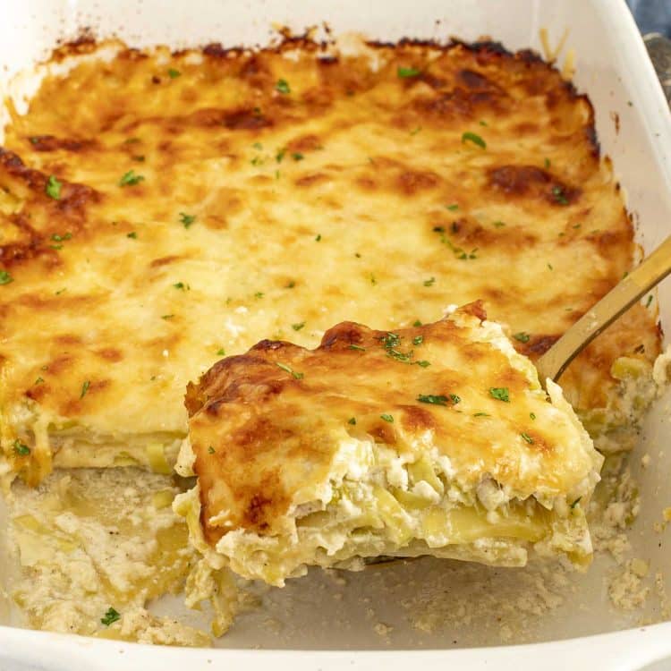 Creamy Gruyère and leek scalloped potatoes being lifted from the baking dish, showing tender layers and browned cheesy top.
