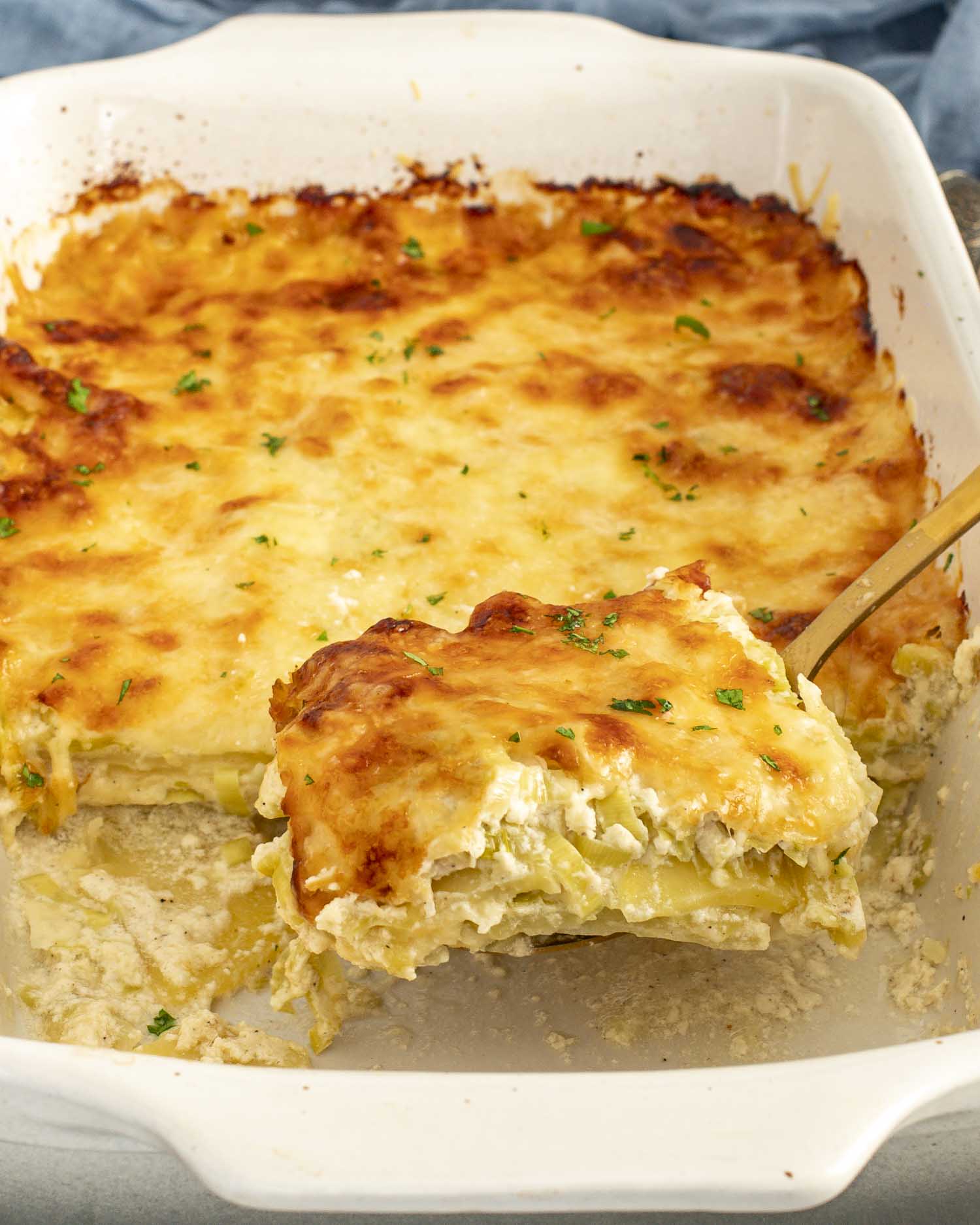 Creamy Gruy&egrave;re and leek scalloped potatoes being lifted from the baking dish, showing tender layers and browned cheesy top.