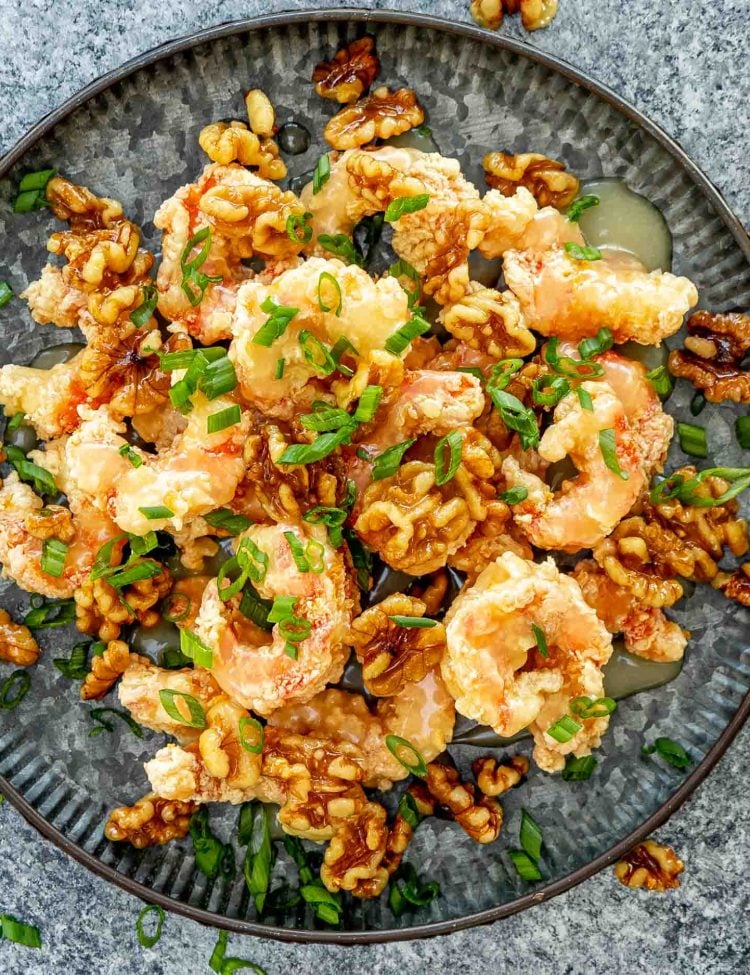 crispy honey walnut shrimp on a metal plate garnished with green onions.