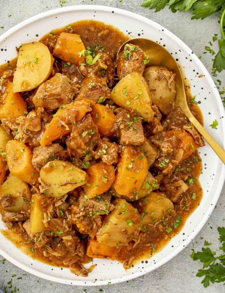 Bright, top-down shot of hearty pork roast with baby potatoes and carrots in rich tomato gravy, sprinkled with parsley.