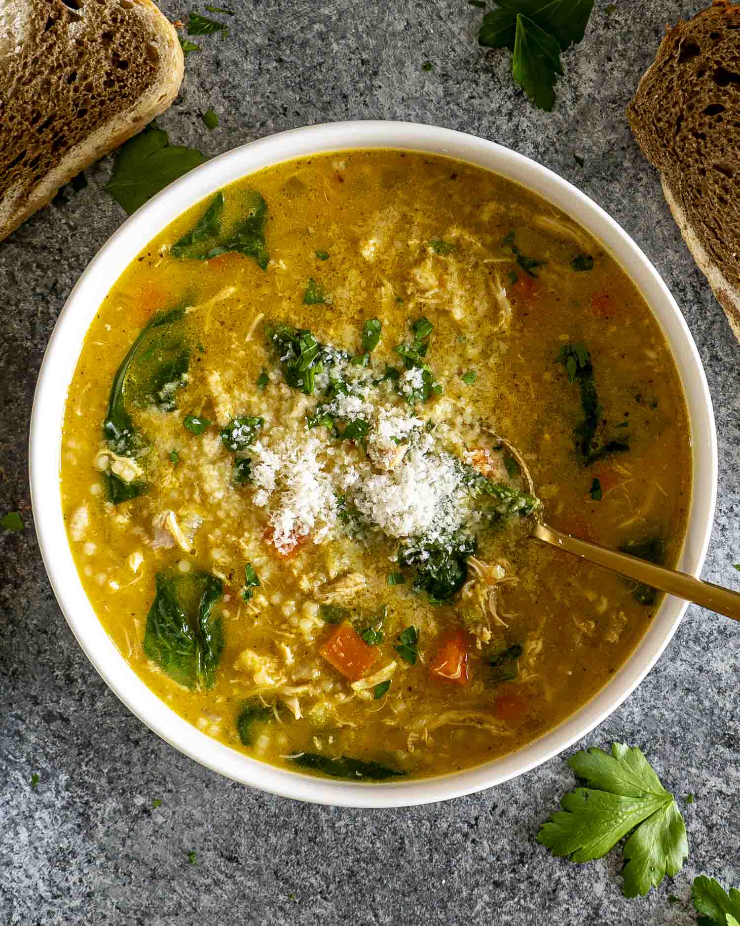 Bowl of Italian Penicillin Soup topped with Parmesan and parsley, served with crusty bread on a dark stone background.