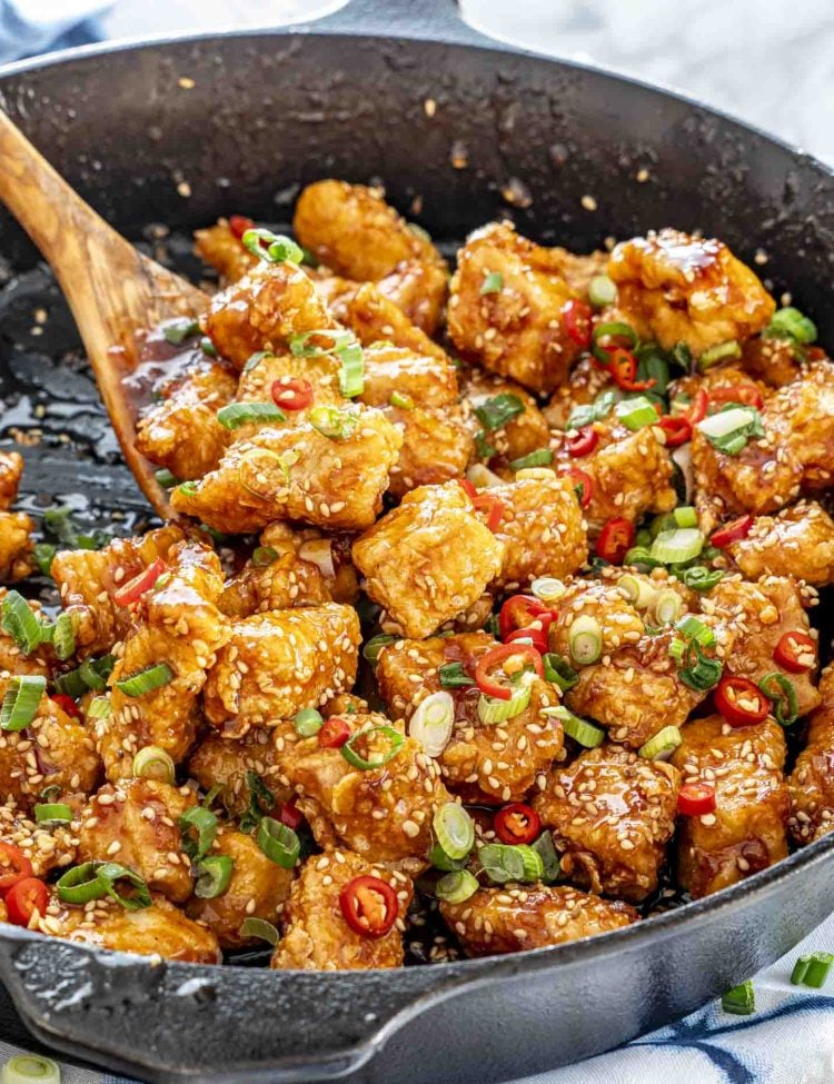 A wooden spoon tossing Korean fried chicken in a skillet