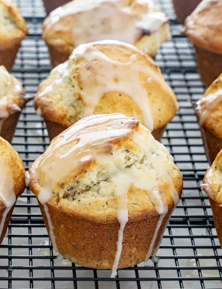 Close-up of freshly baked lemon poppy seed muffins on cooling rack, golden tops dripping with shiny lemon glaze.