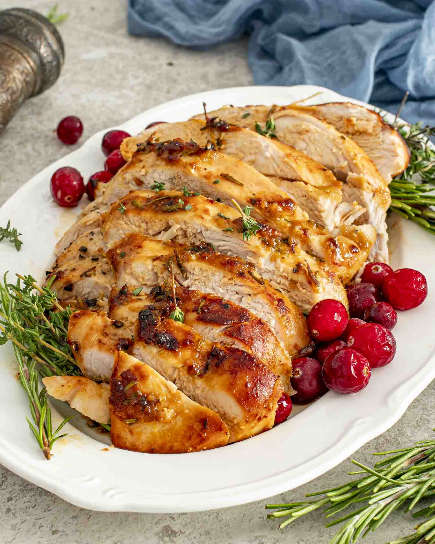 Juicy slices of Maple Dijon Glazed Turkey Breast arranged on a platter with rosemary, thyme, and bright red cranberries.