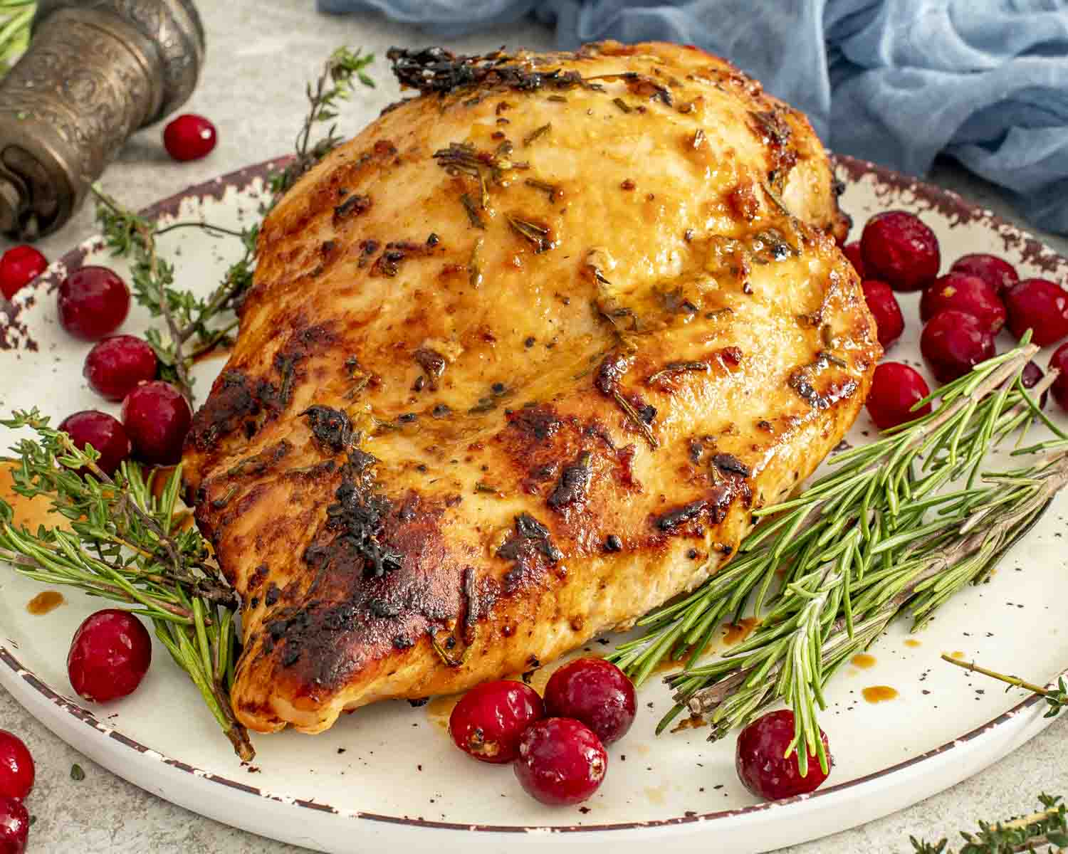 Golden roasted Maple Dijon Glazed Turkey Breast on platter with rosemary, thyme, and cranberries, ready for carving.