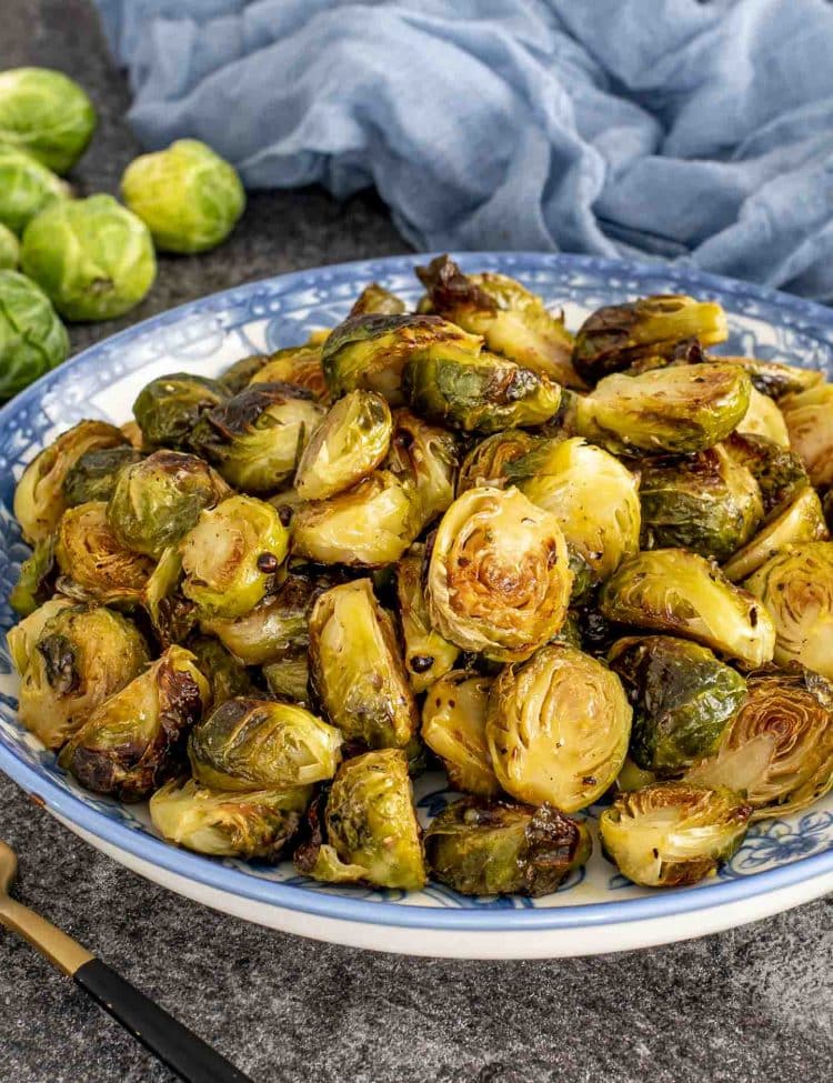 Close-up of crispy Maple Dijon Roasted Brussels Sprouts coated in a sweet and tangy glaze served in a patterned blue bowl.