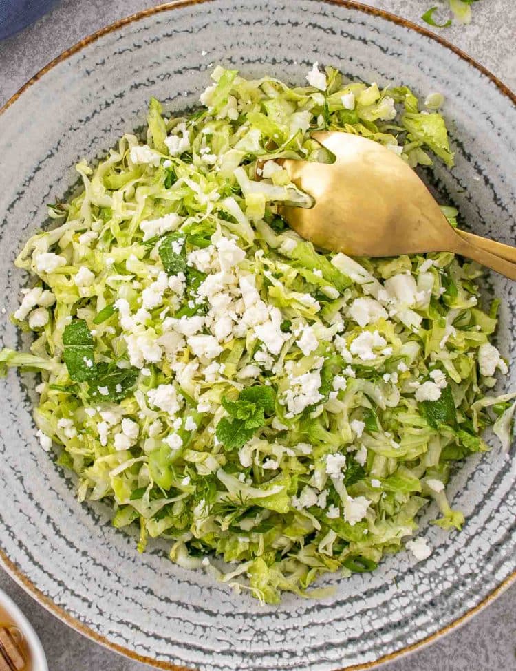 Fresh Maroulosalata topped with feta, surrounded by mint leaves, lemon halves, and honey for garnish.