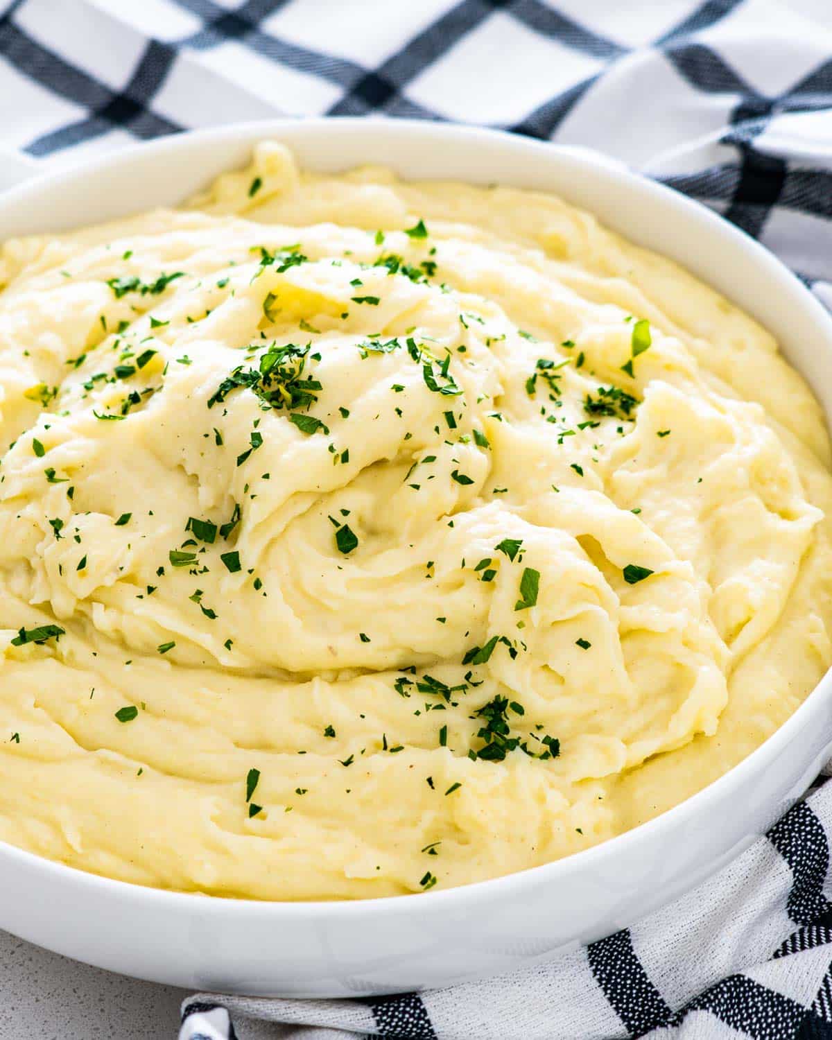 creamy mashed potatoes in a white bowl garnished with parsley.