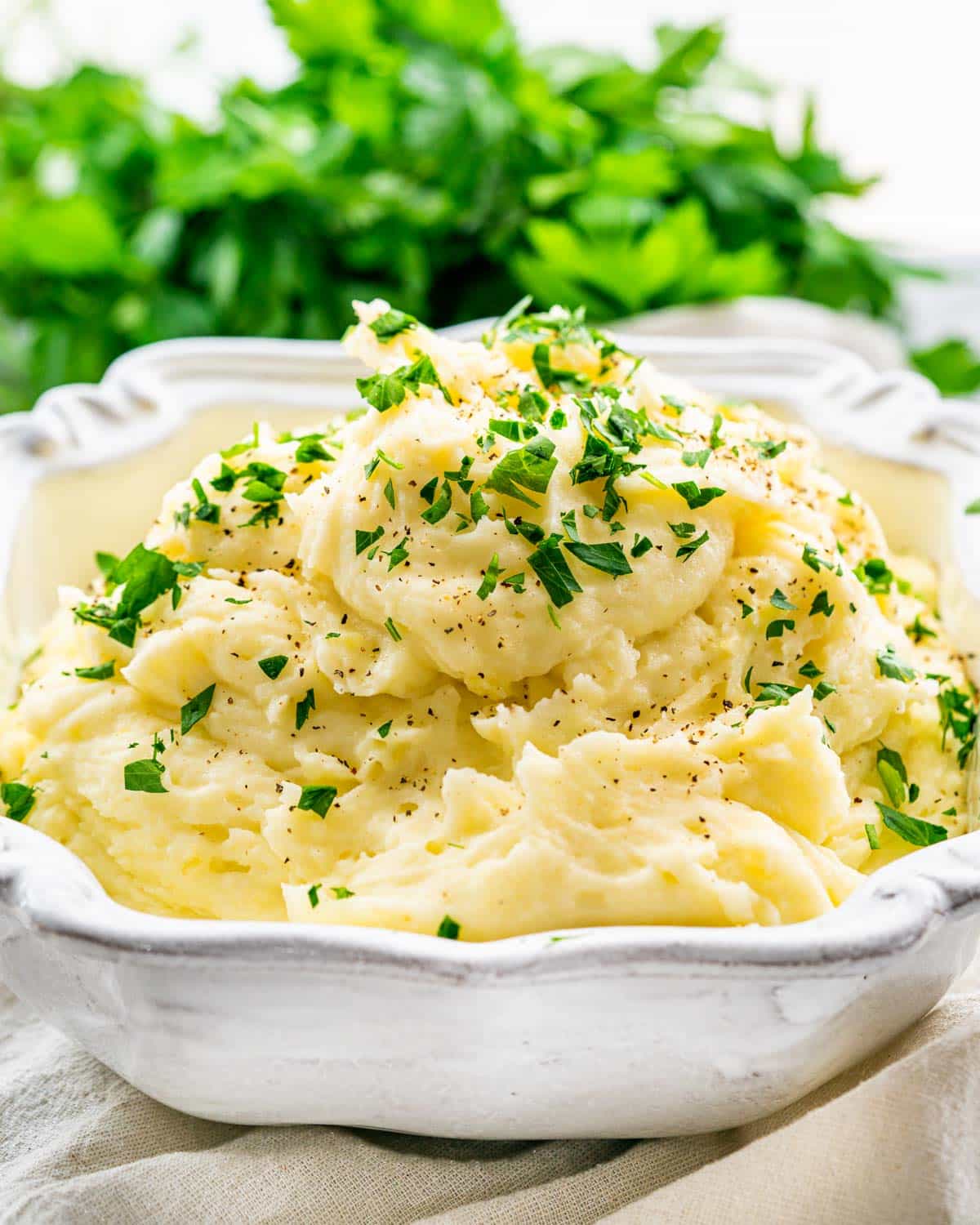 creamy mashed potatoes in a white bowl garnished with parsley.