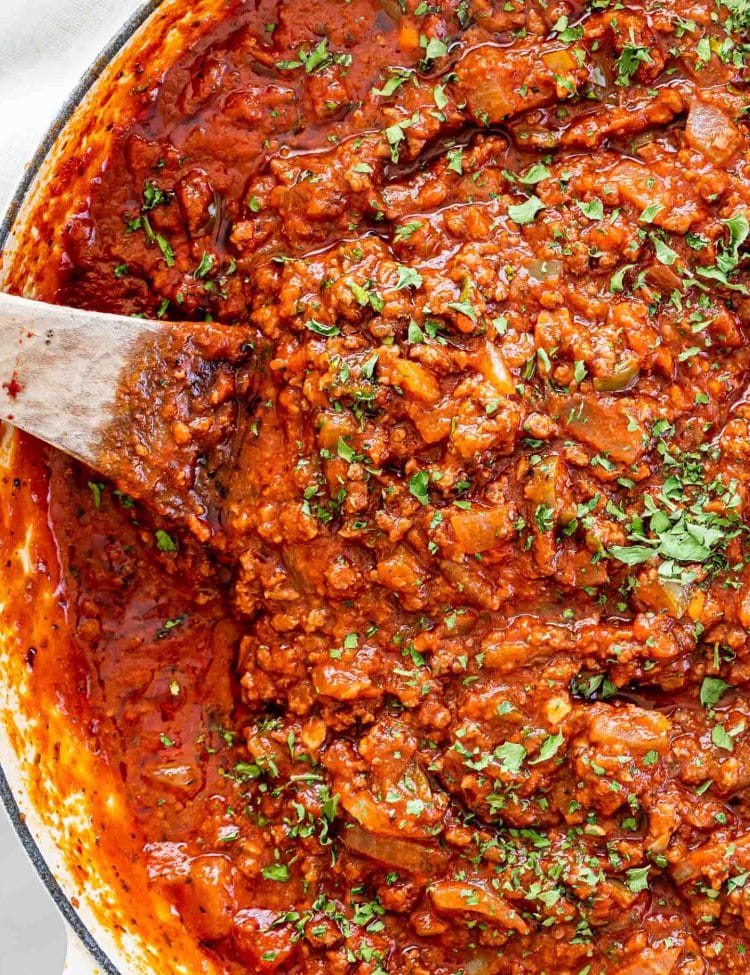 meat sauce in a braiser with a wooden spoon in it and garnished with parsley