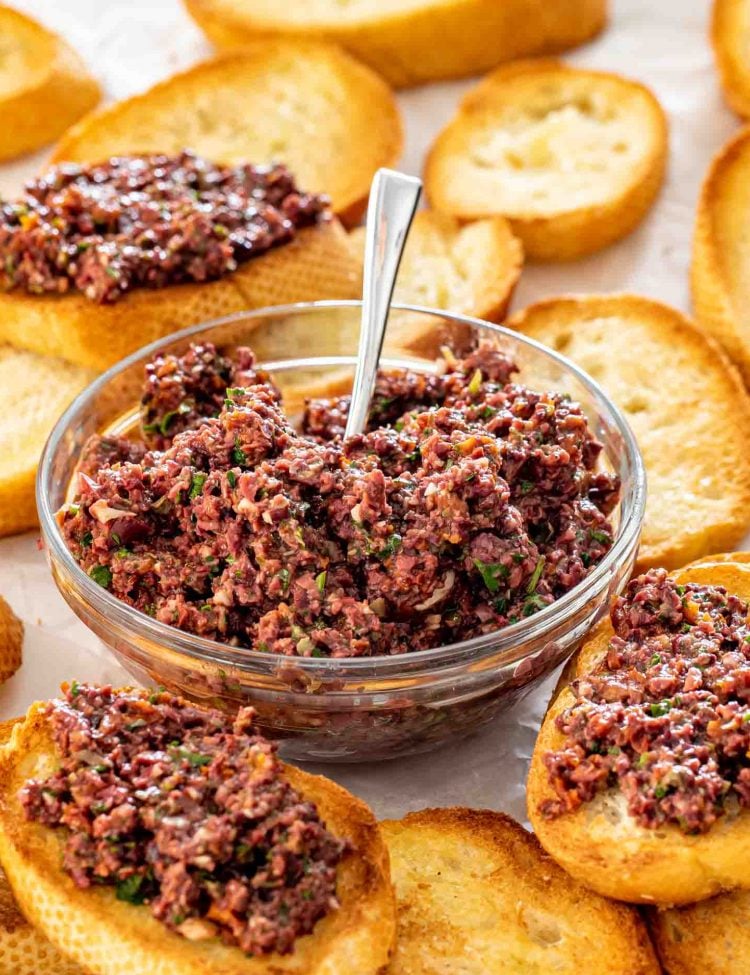 a bowl with olive tapenade surrounded by crostini.