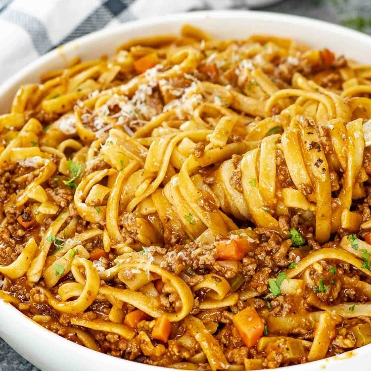 beef ragu pasta garnished with a bit of parsley in a white serving bowl.