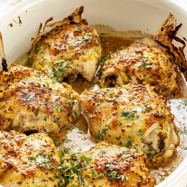 Freshly baked chicken thighs in white casserole dish, coated in golden honey mustard glaze with herbs.