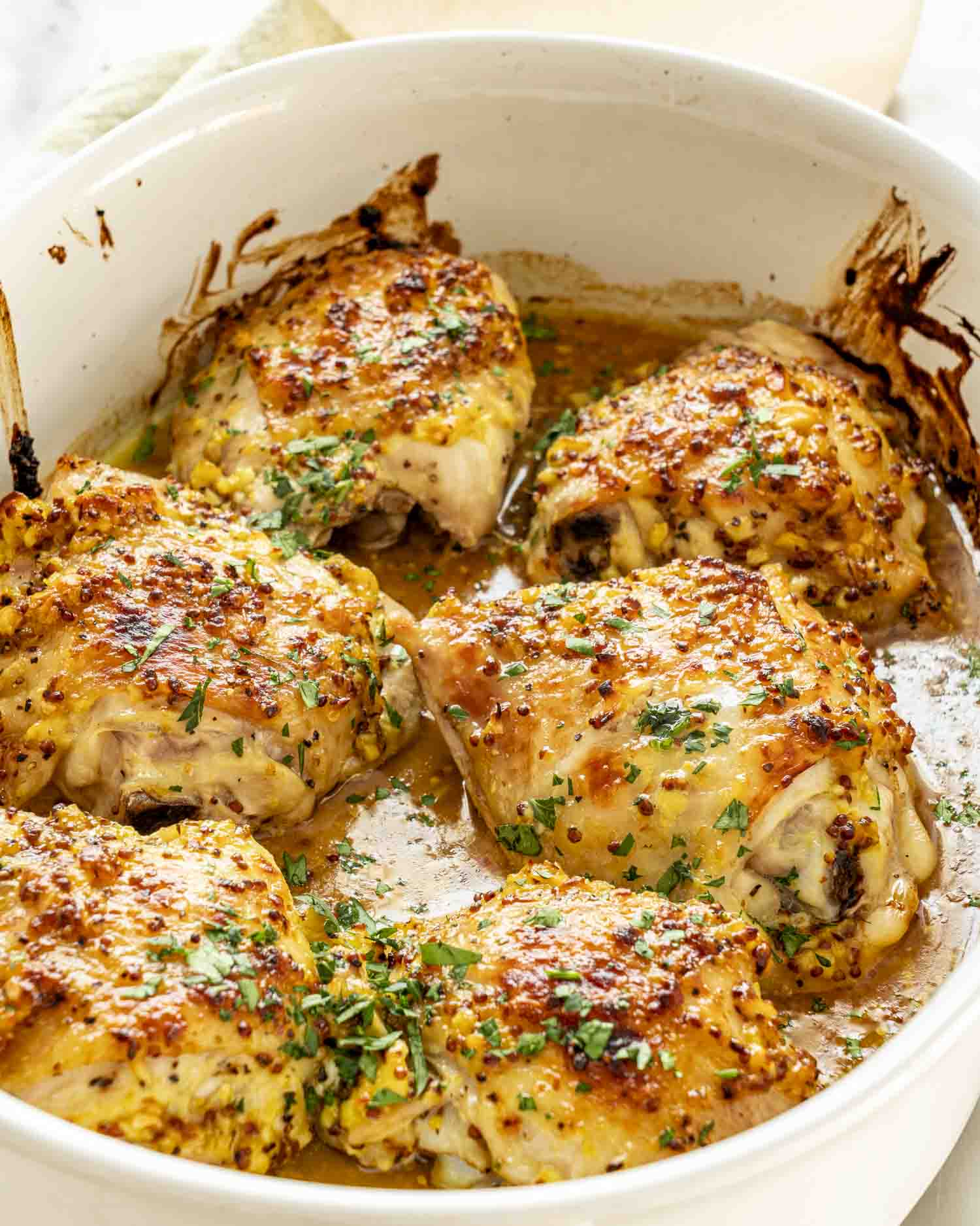 Freshly baked chicken thighs in white casserole dish, coated in golden honey mustard glaze with herbs.